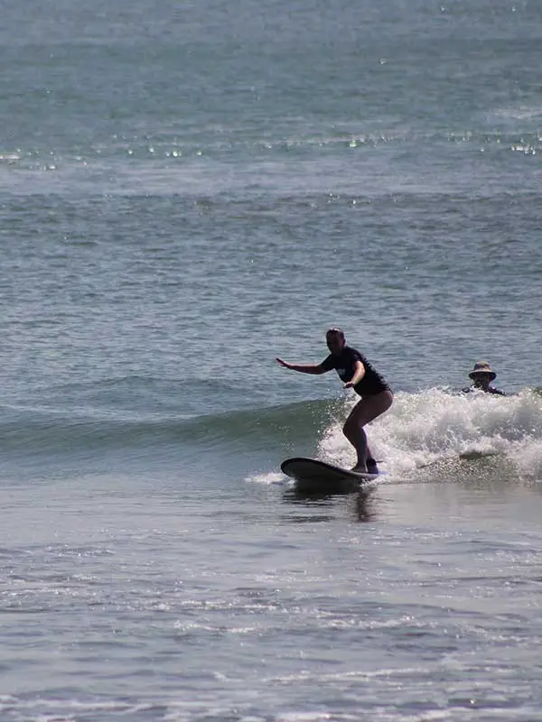 A surfer student surfing a wave while Santi is behind watching how she is enjoying the wave!